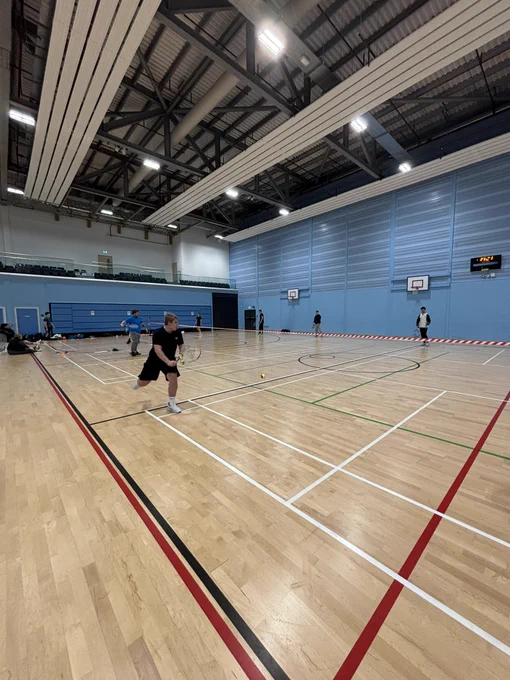 Class of students playing tennis in a sports hall. 