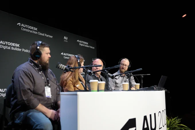 Four people recording a podcast at the Autodesk University 2023 event. They are seated at a table with microphones and laptops, engaging in a discussion.
