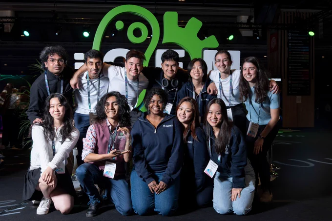 Members of the iGEM Toronto team post together with their best model award. They are standing in front of the logo for the competition which is green and white. The group is arranged into two rows, the back row has seven people standing and the front row has five kneeling.