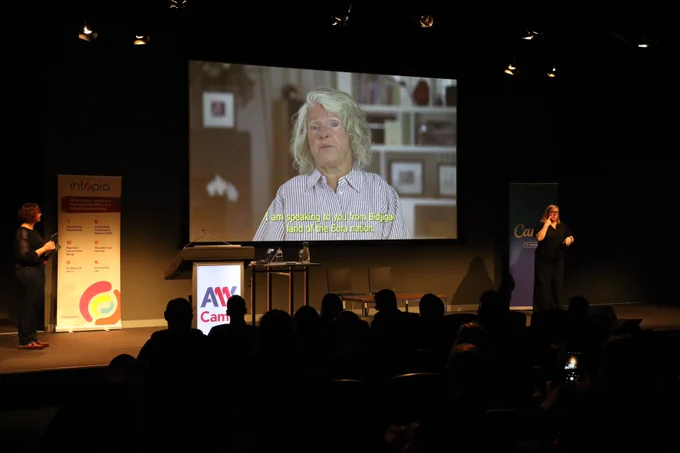 Rosemary Kayess addressing the conference on the big screen. An Auslan interpreter is on the right of stage.