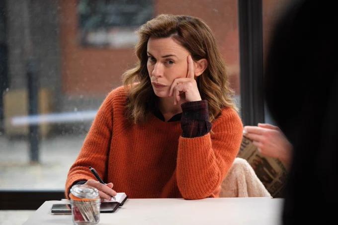 Eve Myles as DCI Jeanette Kirkland in The Crow Girl in an orange sweater sitting at a table, looking thoughtfully out a window with a coffee cup in front of her.