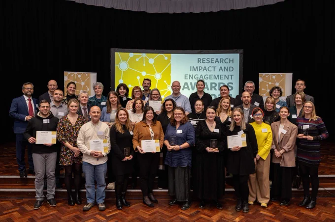 Research Impact and Engagement Award winners and special mentions stand together in front of a sign with the award ceremony title.  