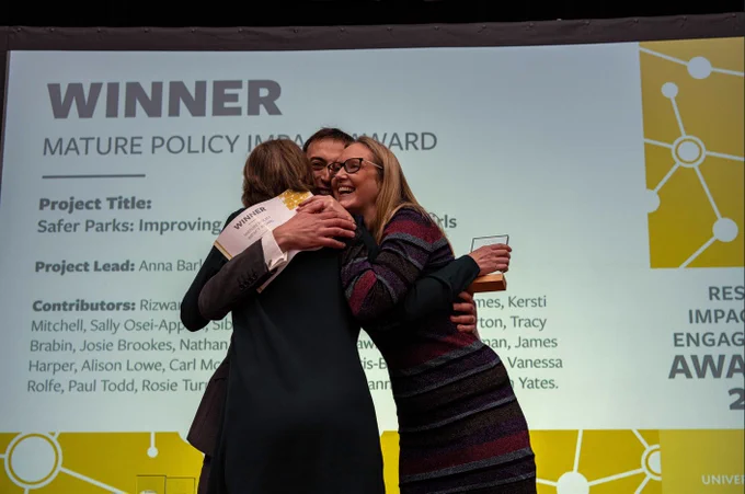 Dr Anna Barker and team share a hug on stage as they celebrate their award win for Mature Policy Impact.