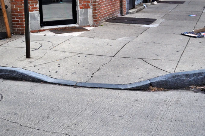 A curb cut (lowered edge of a curb) as an example of something that enables some and supports many.
