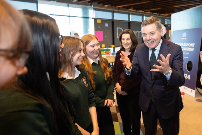 group of young female students smiling, a man in a suit is saying something in an animated way