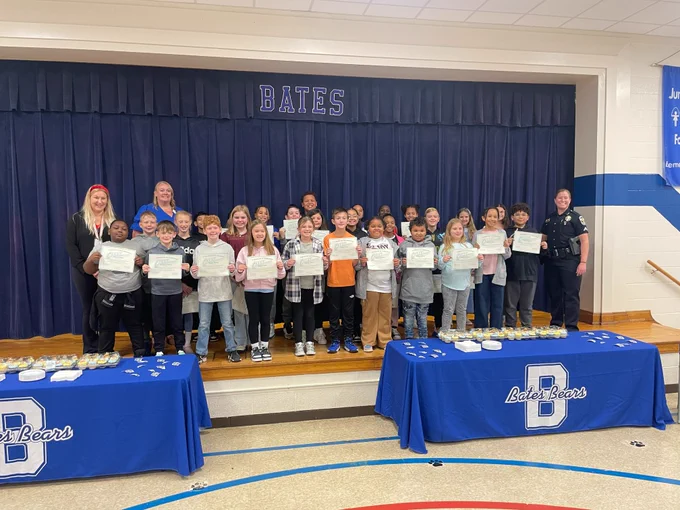 Students and adults pose for a picture on stage. Students hold certificates.