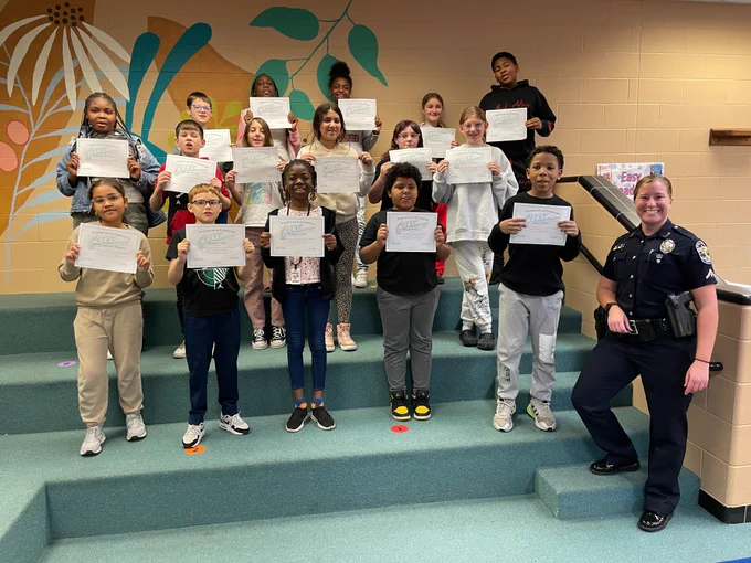 Students and a police officer pose for a picture. The students hold certificates. 