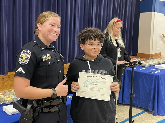 A police officer poses for a picture with a student who is holding a certificate.