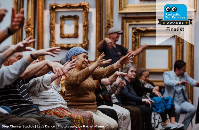A hall of older people sit raising there arms for a creative workshop led by Let's Dance at Step Change Studios, Westminster.