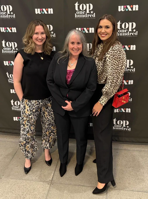 Our Compass Rose team - Kat, Marci and Andrea standing and smiling at a step and repeat. 