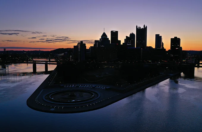 Point State Park and downtown Pittsburgh seen at dawn from a drone. The rising sun is in the background, behind the city. 