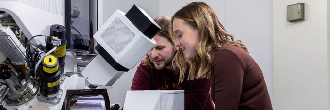 Two colleagues stood looking at a machine, involved in research. 