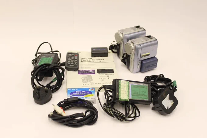 A set of 2 Sony DCR PC-105E camcorders and accessories, including batteries, wires, a manual and more.
