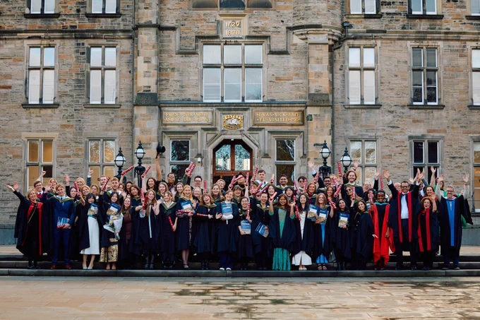 Group of students wearing graduation gowns and holding their scrolls aloft.