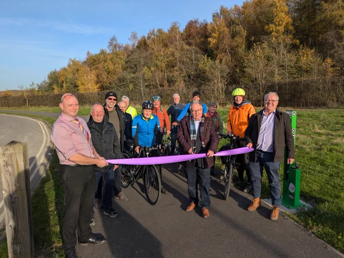 Gentleman cutting a ribbon to open a new cycleway flanked by colleagues and cyclists. 