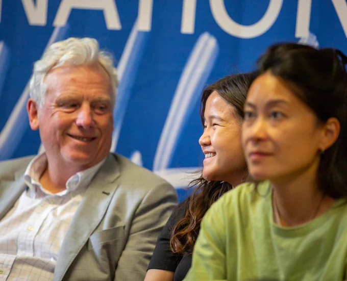 Three people sitting in front of a banner smiling and engaged in a conversation.