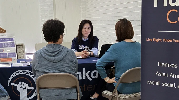 Savinna, Hamkae Center staff, speaks with 2 Korean community members at a table during a Hamkae Center services tabling event.