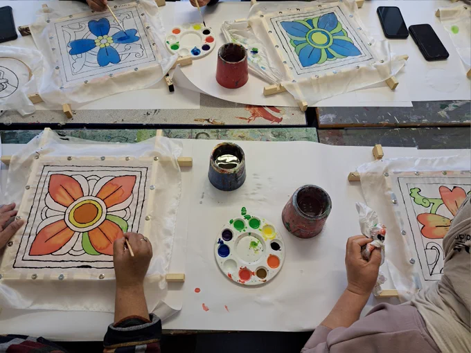 A table at an arts studio with pots of water and loads of hands working on painting silk fabric.