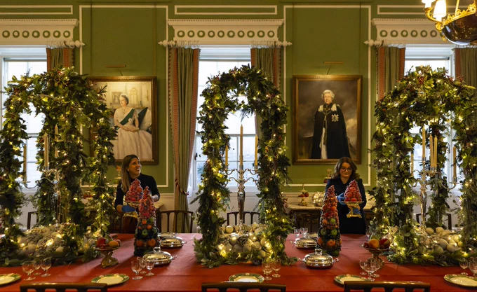A festive dining room with a long table, decorated with garlands and lights. 
