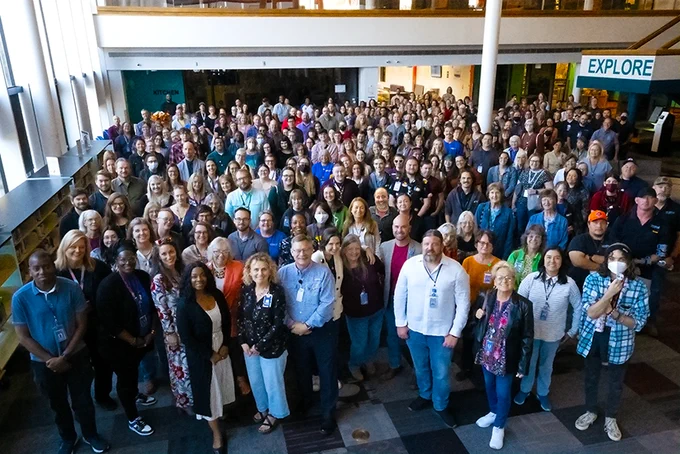 Nearly 300 Library staff members stand together in the lower level of Library 21c for a group photo.