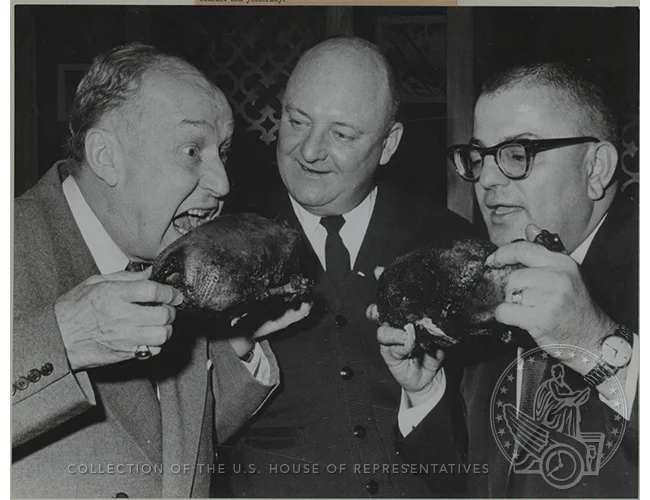 Three men stand with turkey legs about to bite into them
