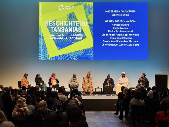 A panel in front of an audience. In the background projected “Histories of Tanzania”.