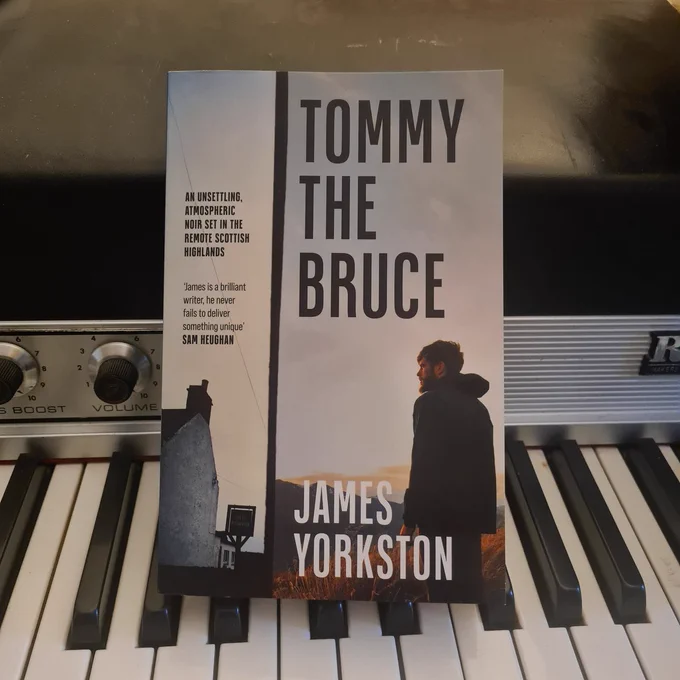 A paperback copy of Tommy the Bruce sits on the keys of a Fender Rhodes keyboard. Tommy will also be available soon as an audiobook, read by JY.