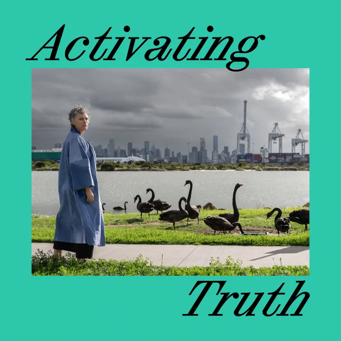 This tile is aqua and has text and a photo on it. The photo is by Jody Haines and is called 'Blak Swan' from the series 'Flowing with the Future (Surviving Batman)', 2024—it shoes Jody standing in the foreground, dressed in sky blue. Next to her are see black swans, gathered on a riverbank. Across the river you can see the city and the port full of containerships and cranes. The sky is cloudy and grey.  The text reads 'Activating Truth'. 