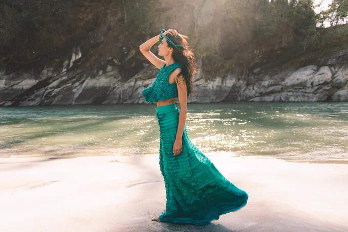 Photograph for a fashion designer. Photograph has a model in the wearing designer teal/green designer skirt and a top. She is standing on the bank of the river Teesta, in the town of Sevoke, West Bengal. The river is visible in the background and on the other side of the river are rocks and the Mangpong Forest.
