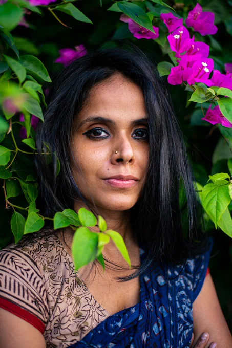 A portrait of writer and translator Meena Kandasamy. She is standing in front of a Bougainvillea tree and looking directly into the camera.