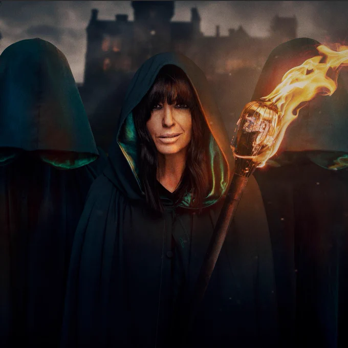 Claudia Winkleman wears a hooded cloak, holding a blazing torch and surrounded by other hooded figures