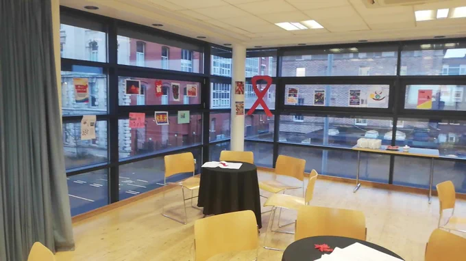 An image of a room in our building with round tables. Posters for world aids day are on the windows.