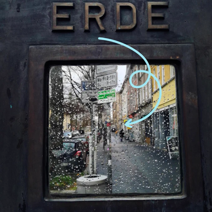 Under the headline "Erde" (that is, German for "Earth") is an artistic rendition of "Earth" as a tiny metal ball between two sheets of glass. An added blue arrow points to the ball because it is really small