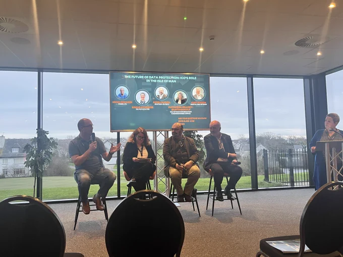 Three men and a woman sat on chairs for a panel discussion with one man talking into a microphone
