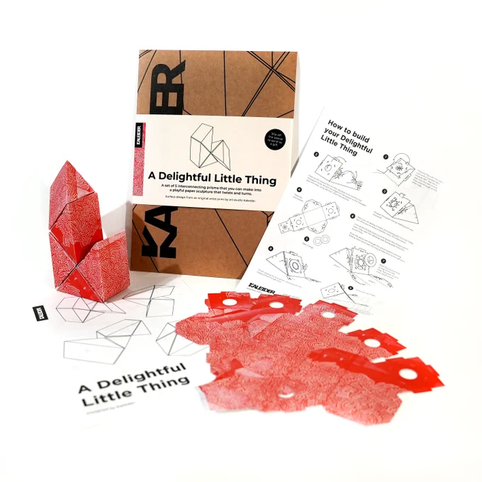 A product shot of Kaleider's Delightful Little Things against a white background. It shows a cardboard envelope package, a sheet of instructions printed on both sides, a set of five flat cardboard cutouts before assembling, and an assembled set.