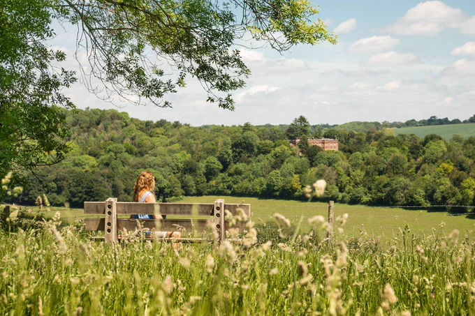 Woman sitting on a bench looking out over fields.