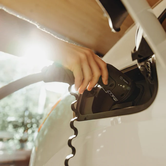A person plugging an EV charger into a white electric car with the sun shining in the background.