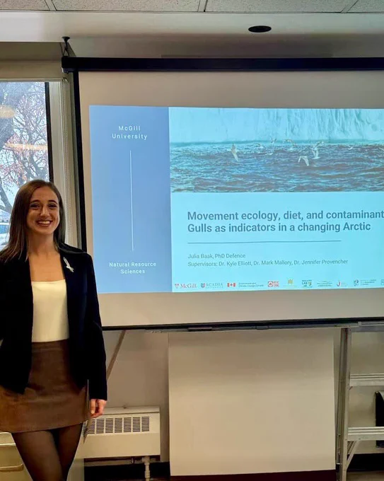 Photo of Julia Baak standing in front of her PhD thesis defence presentation, titled “Movement ecology, diet, and contaminants: Gulls as indicators in a changing Arctic”