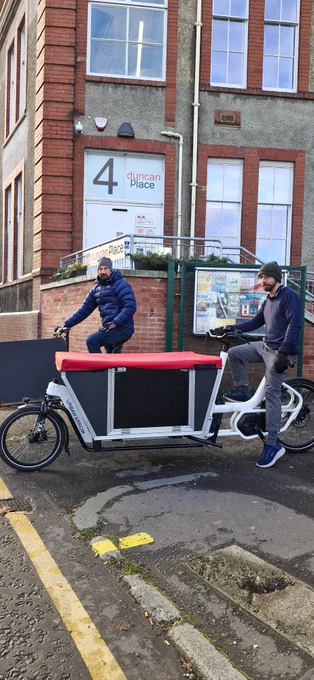 Two people sitting on cargo bikes in front of Duncan Place.