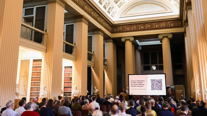 A large gathering sitting within the beautiful Playfair Library Hall, at The University of Edinburgh, in a lecture, facing a screen that reads "Active Lifestyles: a high impact, low cost mental health solution". SAMH's logo is also visible on the screen.