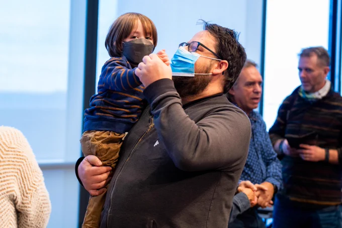 Adult holding a child, both wearing masks, dancing at the JFK Library.