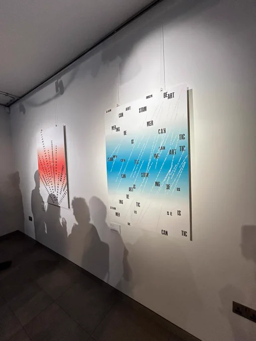 Photograph of two posters created by Conor Foran for the ‘Wouldn’t you rather talk like us?’ art exhibition.  The shadows of exhibition visitors are captured on the white wall