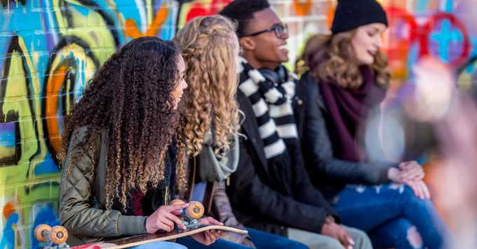 A group of teen sitting together against a wall covered in colourful art