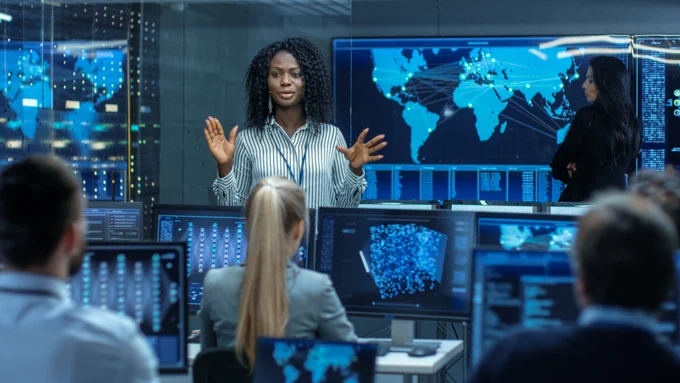 A woman addresses a room full of people on computers.