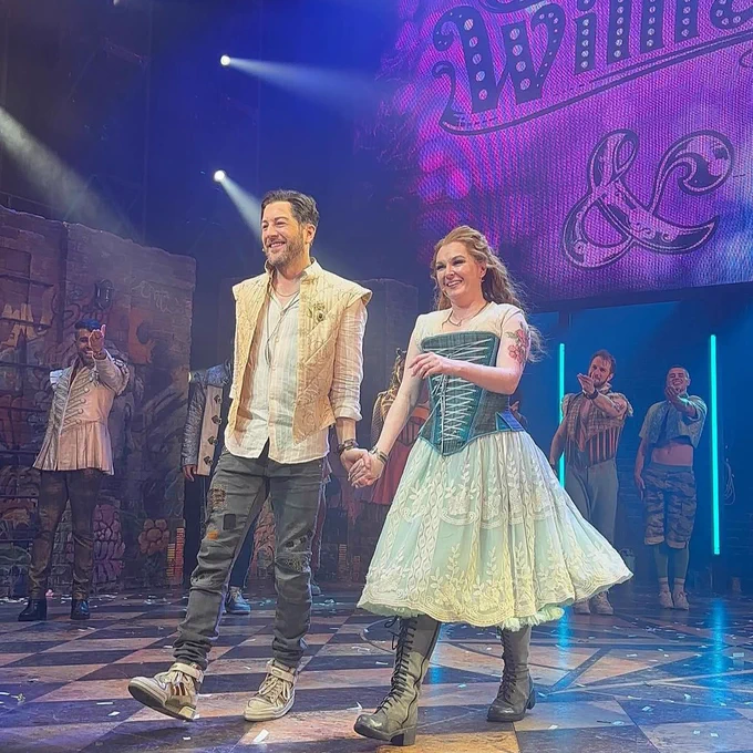 Matt Cardle and Lara Denning onstage in the bows, smiling and holding hands.