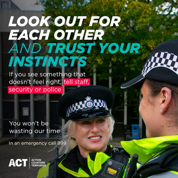 The foreground features a smiling, female police officer, her gaze directed slightly towards the viewer.  She is wearing a police uniform jacket, a peaked cap with a checkered pattern.  The lettering on the top of the image, "LOOK OUT FOR EACH OTHER AND TRUST YOUR INSTINCTS,". Below that, additional text in black gives advice on noticing suspicious activity and reporting it to security or police and advises against wasting their time. The text "In an emergency call 999" is prominent, as well as the "ACT" logo and its description below.

A second female police officer, is partially visible behind and slightly to the right of the first officer.  The background includes a slightly blurred view of a building exterior