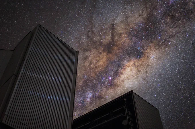 Aus dem perspektivisch dreieckigen geöffneten Kuppelspalt eines VLT-Teleskops ragt das helle Band der Milchstraße