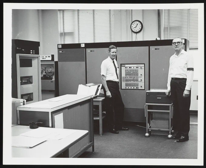 Courtesy of Science History Institute, credits to: Henry Earle Lumpkin Photograph Collection.

View of the IBM 1800 computer used to accept and process data from a mass spectrometer at the Exxon Research and Engineering Company laboratory in Baytown, Texas. This photograph was taken on the day that use of the computer was discontinued at the laboratory. Henry Earle Lumpkin (Research Associate in charge of computer operations) stands to the left while laboratory technician Jack L. Taylor is visible on the right. Taylor is wearing a black band on his right arm to mark the "death" of the computer.