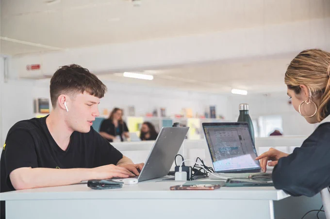 A man and a woman working on a laptop on opposite sides of a table 