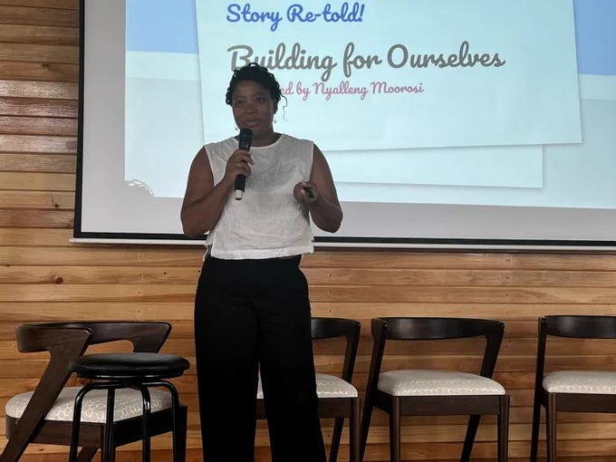 Nyalleng stands in front of a screen presenting her keynote. A presentation in the background says "Building for ourselves".